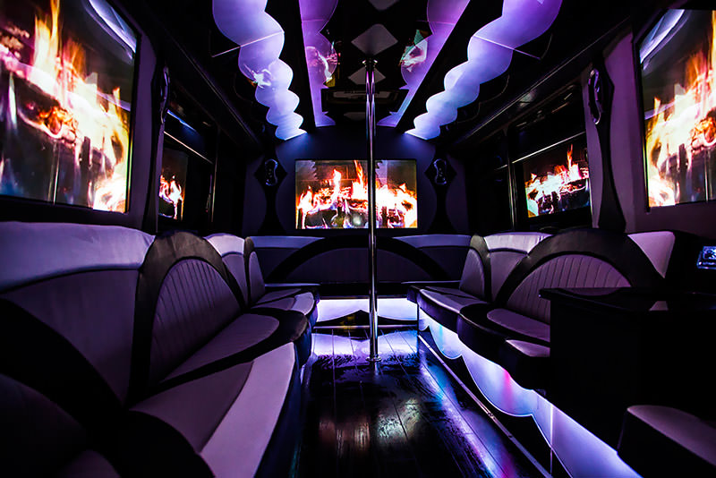 The colorful purple lights and fireplace view on the televisions really sets the ambiance in this party bus interior view.